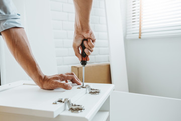 Happy asian man home improvement Assembling Furniture Reads Instructions and Tightens Screw with a Drill. Moving into New House Renovation concept