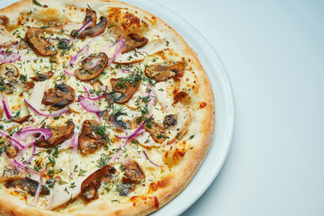 Appetizing baked Italian pizza with cream sauce, onions and mushrooms on a white plate isolated on gray background