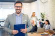 © Bojan - Smiling businessman holding folder in office