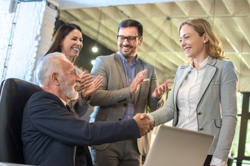 Smiling mature businesswoman handshaking with senior businessman at meeting negotiation. Colleagues clapping hands and celebrating successful agreement