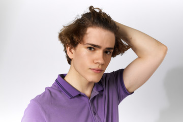 Wall Mural - People and lifestyle concept. Horizontal portrait of handsome young European male wearing violet polo shirt looking at camera touching his voluminous hair, having serious facial expression