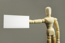 Wooden Figure Holding Empty White Poster In Hand On Grey Background