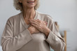 © fizkes - Close up middle aged happy woman thanking God with folded hands on heart, Grateful sincere smiling senior older grandmother holding hands on chest feeling excited by good news, believe faith concept.