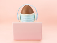 A Chocolate Egg In Headphones And In A Medical Face Mask Sits At A Computer,laptop. Easter Concept 2020,covid-19,online Celebration
