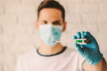 Man in protective mask on face and medical gloves holding digital thermometer in hand. Professional doctor showing electronic thermometer with normal body temperature. Coronavirus COVID-19 prevention