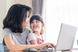 © Kawee - Asian young mother work from home. Woman use laptop for meeting with colleague while daughter sit on the lap and smile. Mom happy to do job while taking care family. Covid-19 Social distancing concept