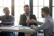 © fizkes - Successful businessman in suit shaking hand of business partner at company meeting. Diverse team fasten deal with applicant at hire. Leader with african american assistant congratulates clients.