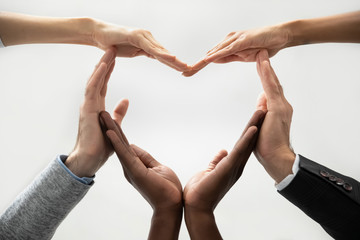 Wall Mural - Close up bottom view concept of diverse business people join hands forming heart. Show unity and support, protection of business. Multiracial colleagues involved in team building activity for charity.