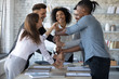 Smiling diverse employees stack fists at corporate meeting, celebrating success, business achievement. Engaged in funny happy team building activity. Colleagues showing unity and support concept.