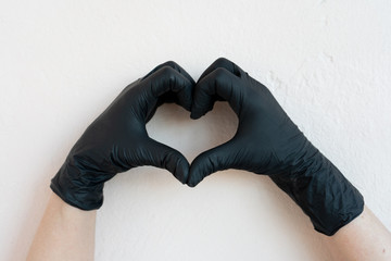 COVID-19, pandemic, two hands in black protective gloves folded in the shape of a heart on a light background