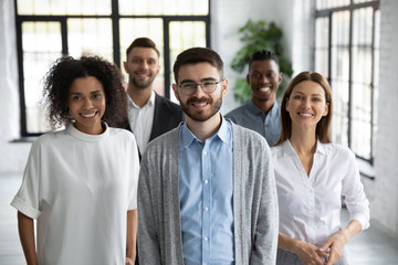 Wall Mural - Close up headshot portrait of three happy diverse businesspeople looking at camera. Different smiling employee standing behind of female and male company mentors. Leader of multi-ethnic team concept.