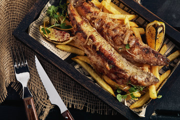 Fish and chips. Classic English food, french fries and fried fish on a wooden board, dark wooden background, food photo.