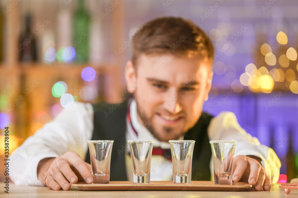 Handsome male bartender with shots of tequila in pub