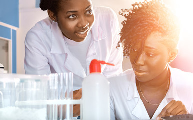 Wall Mural - Two African medics, technical assistants, scientists, young women work in research laboratory, medical test lab. Protein testing in water, pollution research. Panoramic image, light flare.