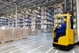 Fototapeta Sawanna - Huge distribution warehouse with high empty shelves and forklift with driver in yellow helmet.