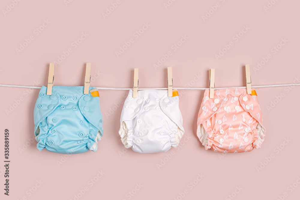 Reusable cloth baby diapers drying on a clothes  line. Eco friendly cloth nappies on a pink background. Sustainable lifestyle. Zero waste concept. - obrazy, fototapety, plakaty 