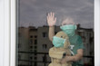 Coronavirus, Covid-19, Boy and his stuffed puppy in protection masks look through the window, quarantine at home 