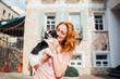 © Elizaveta - The theme is the friendship of man and animal. Beautiful young red hair Caucasian woman holding a pet dog Chihuahua breed near a house building in the summer in sunny weather