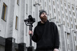 © Volodymyr - Bearded Professional videographer in black hoodie holding professional camera on 3-axis gimbal stabilizer. Filmmaker making a great video with a professional cinema camera. Cinematographer.