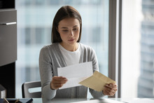 Pensive Young Woman Sit At Desk In Office Open Envelope Read Post Correspondence, Focused Thoughtful Millennial Female Get Postal Letter Consider Offer Or Suggestion, Promotion Or Dismissal Notice