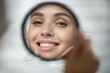 Close up of beautiful young woman look in mirror show healthy white teeth after dental treatment good oral care, smiling millennial female touch clean glowing face skin after beauty procedures