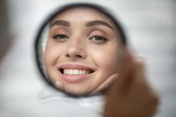 Wall Mural - Close up of beautiful young woman look in mirror show healthy white teeth after dental treatment good oral care, smiling millennial female touch clean glowing face skin after beauty procedures