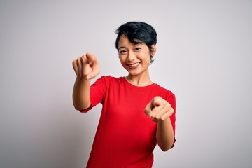 Young beautiful asian girl wearing casual red t-shirt standing over isolated white background pointing to you and the camera with fingers, smiling positive and cheerful