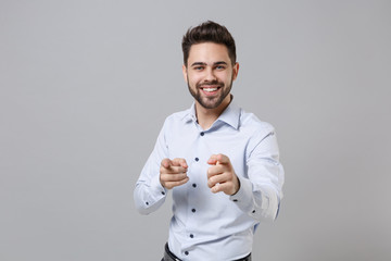 Wall Mural - Smiling successful young unshaven business man in light shirt posing isolated on grey wall background. Achievement career wealth business concept. Mock up copy space. Pointing index fingers on camera.