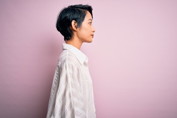 Wall Mural - Young beautiful asian girl wearing casual shirt standing over isolated pink background looking to side, relax profile pose with natural face and confident smile.