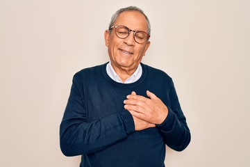 Wall Mural - Senior handsome grey-haired man wearing sweater and glasses over isolated white background smiling with hands on chest with closed eyes and grateful gesture on face. Health concept.