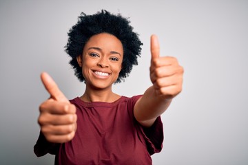 Young beautiful African American afro woman with curly hair wearing casual t-shirt standing approving doing positive gesture with hand, thumbs up smiling and happy for success. Winner gesture.