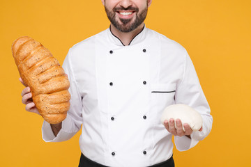 Wall Mural - Cropped image of young bearded male chef cook or baker man in white uniform shirt posing isolated on yellow background studio portrait. Cooking food concept. Mock up copy space. Hold bread, raw dough.