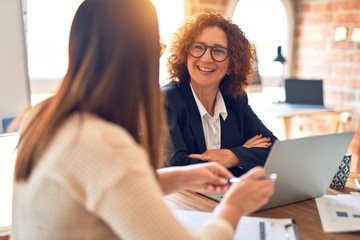 Two beautiful businesswomen smiling happy and confident. Sitting with smile on face working together using laptop at the office