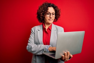 Canvas Print - Middle age curly hair business woman working using laptop over isolated red background with a confident expression on smart face thinking serious