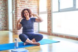 Fototapeta Na drzwi - Middle age beautiful sportswoman wearing sportswear sitting on mat practicing yoga at home smiling cheerful showing and pointing with fingers teeth and mouth. Dental health concept.