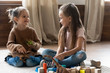 © fizkes - Full length adorable little kids sisters sitting on floor carpet, playing with toys in living room. Happy small girls chatting, having fun together, enjoying spending free leisure time at home.