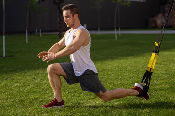 Wall Mural - Young athlete training with suspension band on street