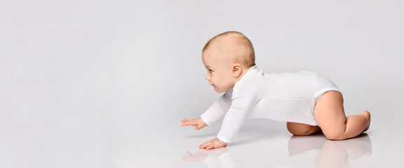 chubby ginger baby boy in bodysuit, barefoot. he smiling, creeping on floor isolated on white backgr