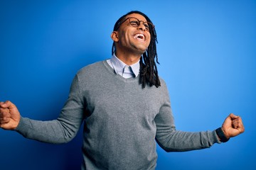 Wall Mural - Young handsome african american man with dreadlocks wearing casual sweater and glasses very happy and excited doing winner gesture with arms raised, smiling and screaming for success. Celebration 