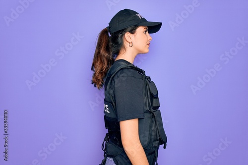 Fotomural Young police woman wearing security bulletproof vest uniform over purple background looking to side, relax profile pose with natural face and confident smile