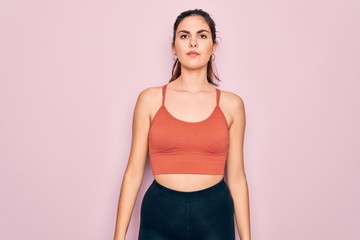 Poster - Young beautiful fitness woman wearing sport excersie clothes over pink background with serious expression on face. Simple and natural looking at the camera.