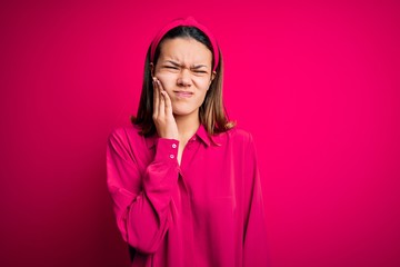 Wall Mural - Young beautiful brunette girl wearing casual shirt standing over isolated pink background touching mouth with hand with painful expression because of toothache or dental illness on teeth. Dentist