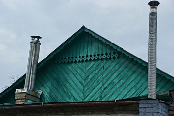 green wooden attic in a rural house with two metal chimneys against a gray sky