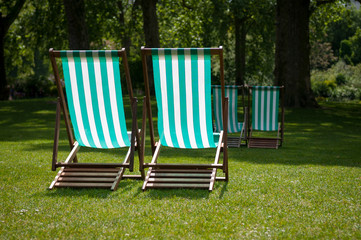 Pair of colorful striped traditional folding deck chairs sitting empty in a sunny green grass park in London, UK