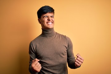 Sticker - Young handsome man wearing casual turtleneck sweater over isolated yellow background excited for success with arms raised and eyes closed celebrating victory smiling. Winner concept.