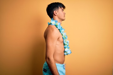 Canvas Print - Young handsome tourist man on vacation wearing swimwear and hawaiian lei flowers looking to side, relax profile pose with natural face with confident smile.