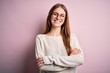 © Krakenimages.com - Young beautiful redhead woman wearing casual sweater and glasses over pink background happy face smiling with crossed arms looking at the camera. Positive person.