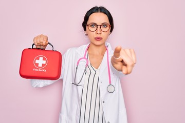 Wall Mural - Young beautiful doctor woman with blue eyes wearing stethoscope holding first aid kit box pointing with finger to the camera and to you, hand sign, positive and confident gesture from the front