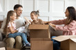 © fizkes - Adorable playful little girl hiding in big cardboard box, while happy parents and sister finding her. Joyful family couple having fun with cute children in living room after moving in new apartment.