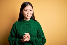 Young Beautiful Asian Woman Wearing Green Winter Sweater Over Yellow Isolated Background With Hands Together And Crossed Fingers Smiling Relaxed And Cheerful. Success And Optimistic